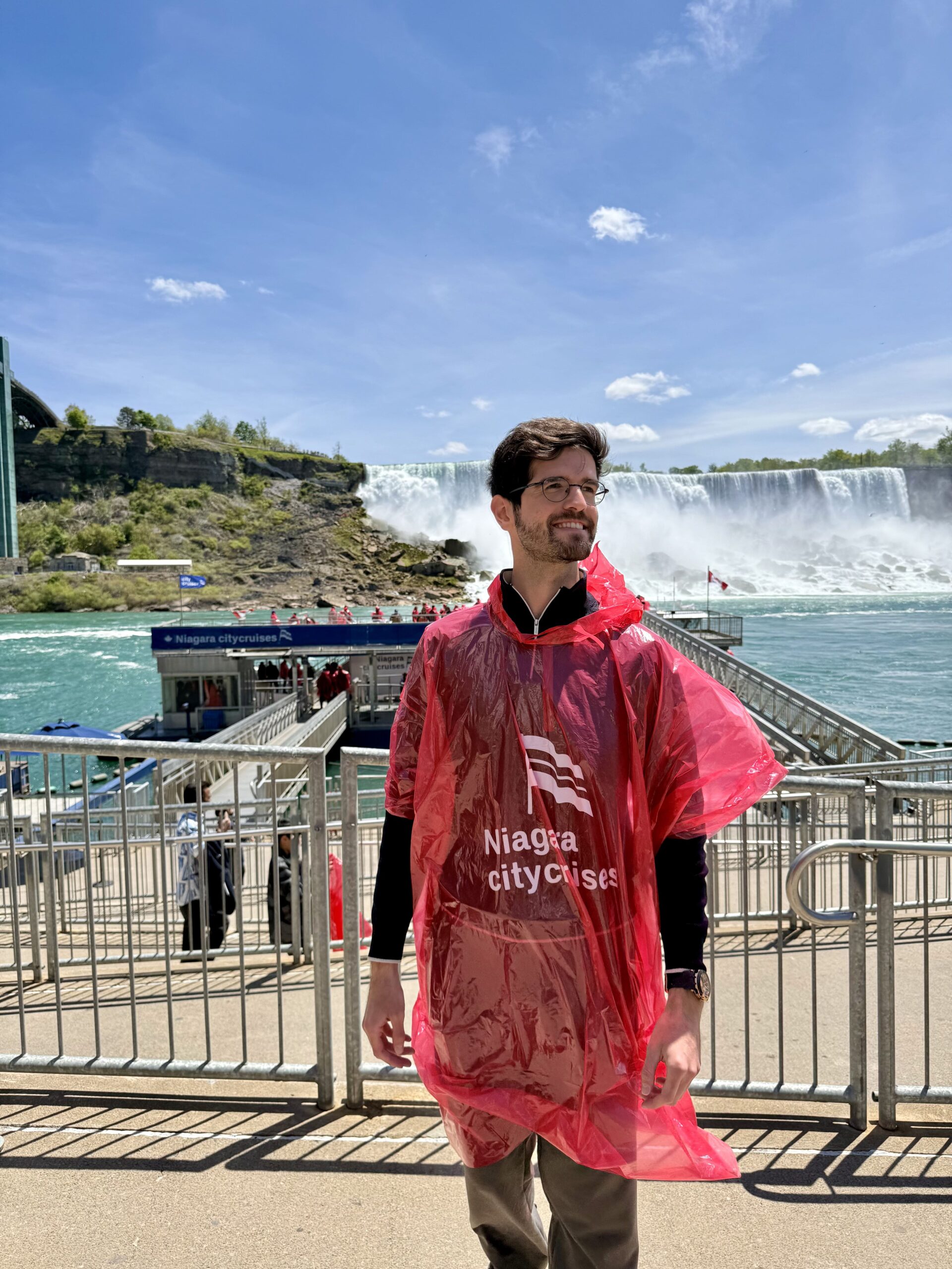 Erhun Abbasli in a red Niagara City Cruises poncho with the American Falls behind him